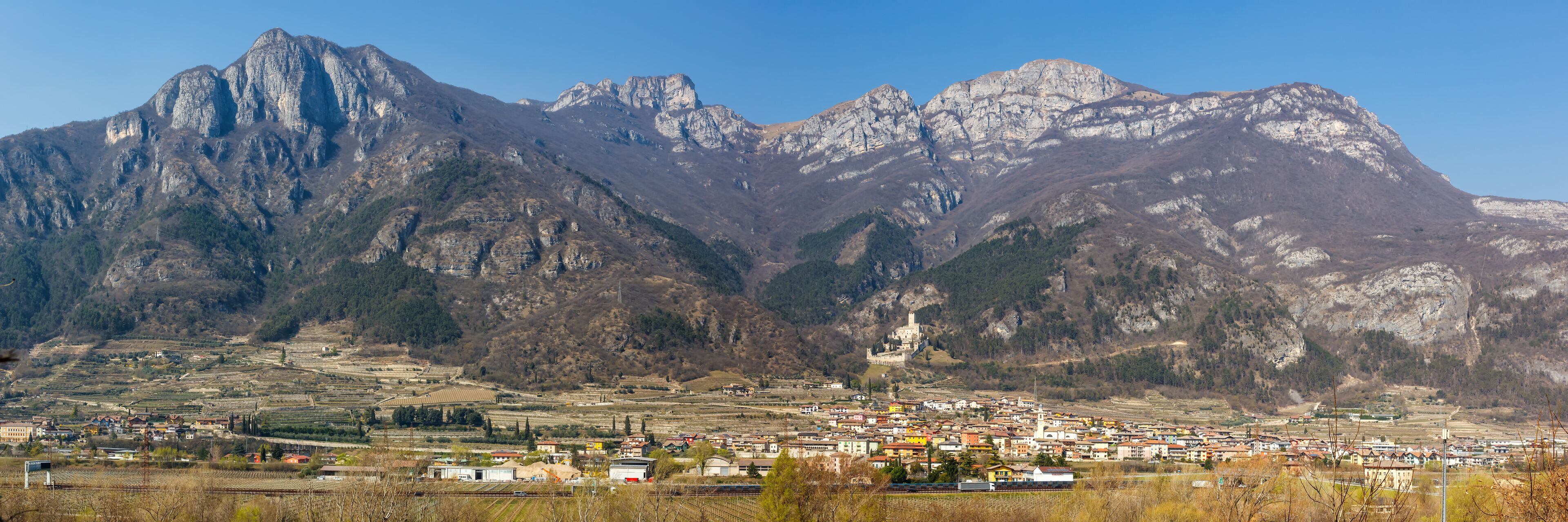 A town nestled in a valley with a prominent castle on a hill and mountains in the background.