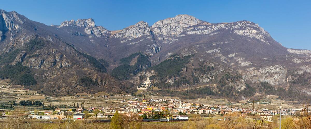 A town nestled in a valley with a prominent castle on a hill and mountains in the background.