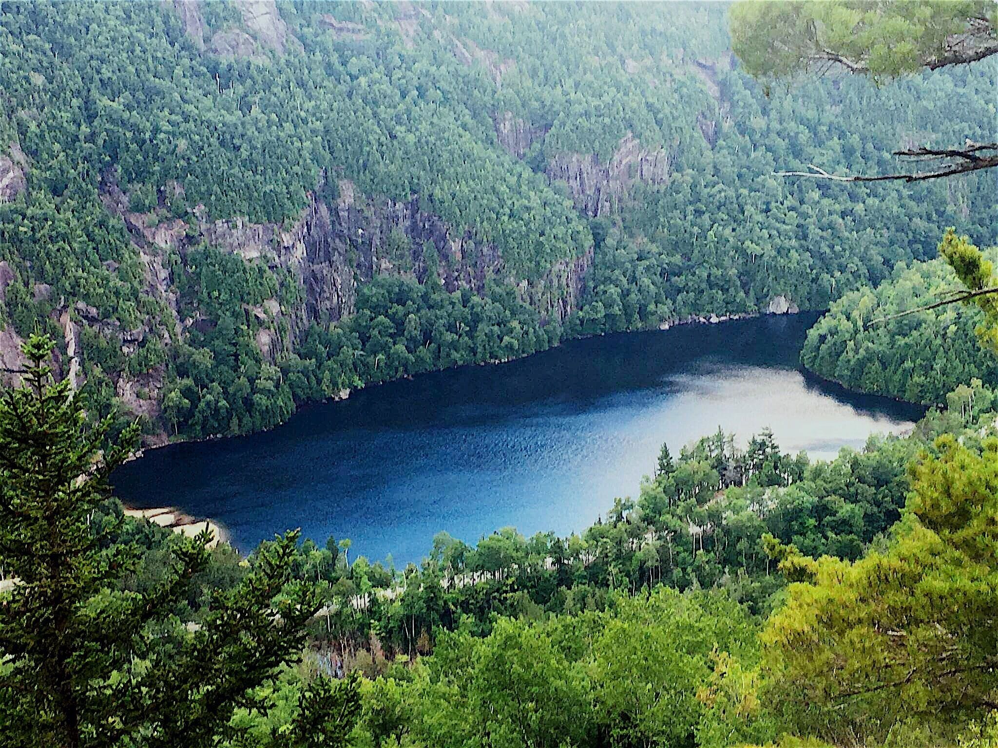 A deep blue lake surrounded by dense forest and rocky cliffs.