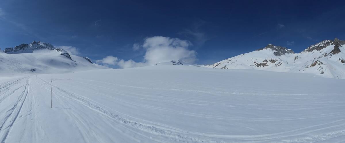 A snow-covered mountain path with rugged peaks and a clear blue sky.