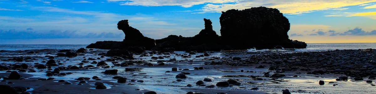 A rocky shoreline with large boulders and a clear sky with scattered clouds.