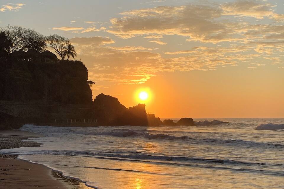 Un atardecer sobre una costa rocosa con olas rompiendo en la orilla.