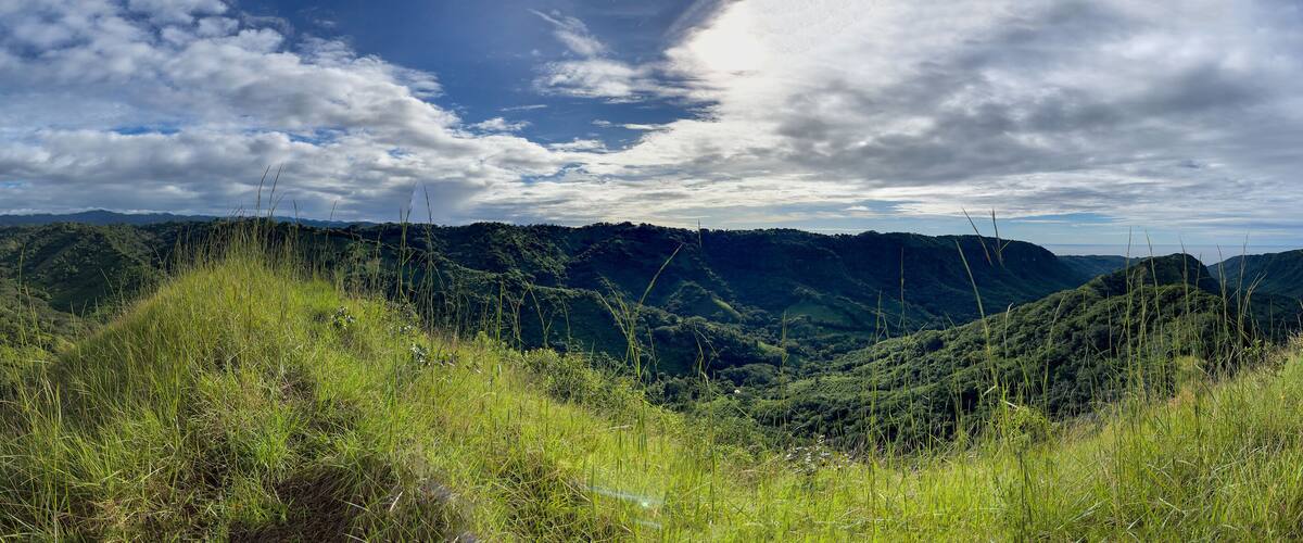 A lush valley with rolling hills and a partly cloudy sky.