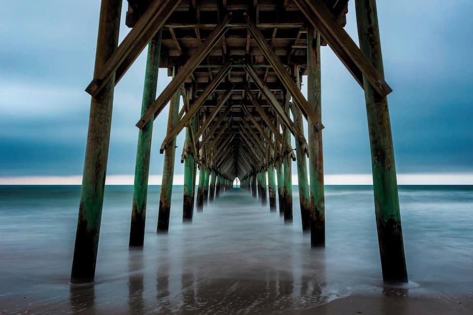 A wooden pier extending into a calm sea under a cloudy sky.