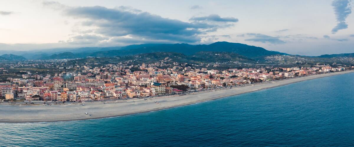 A coastal cityscape with a beach, buildings, and mountains in the background.