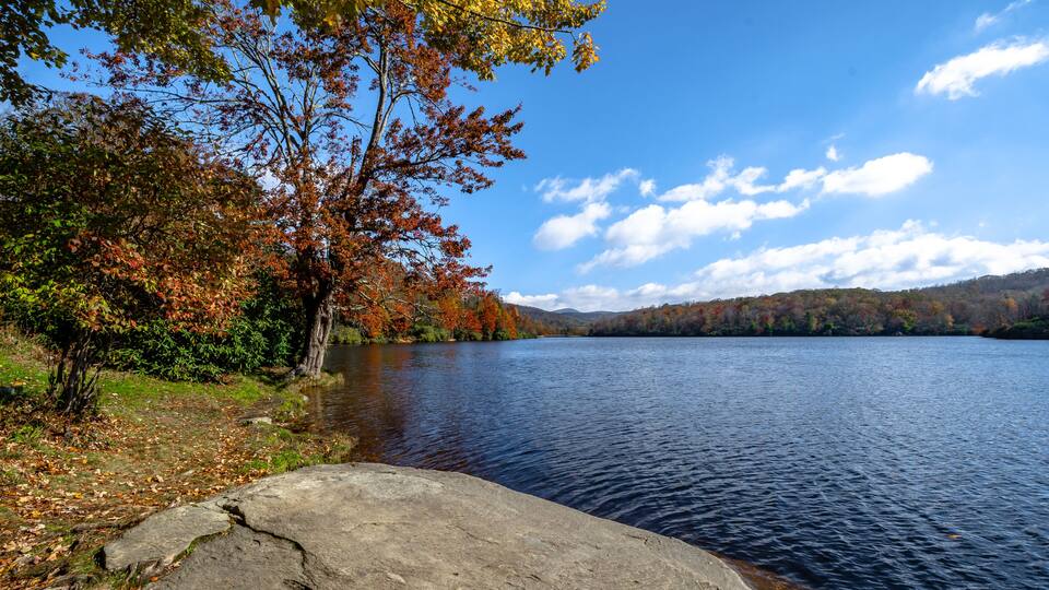 A calm lake surrounded by autumn foliage and distant hills.