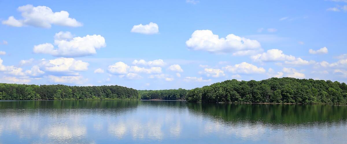 A calm lake with a forested island and a clear sky with scattered clouds.