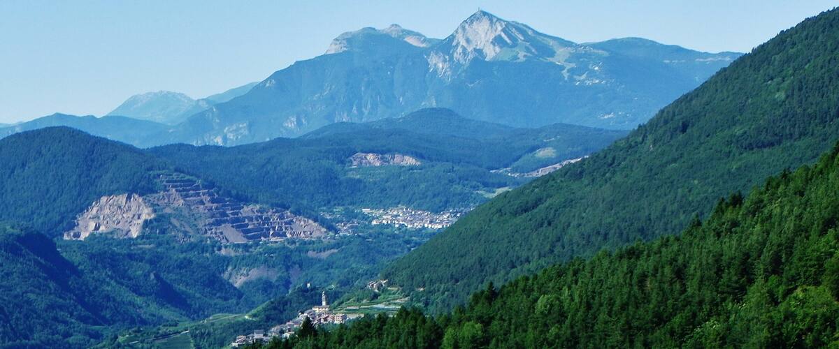A mountainous landscape with a prominent peak, lush green forests, and a small town nestled in the valley.