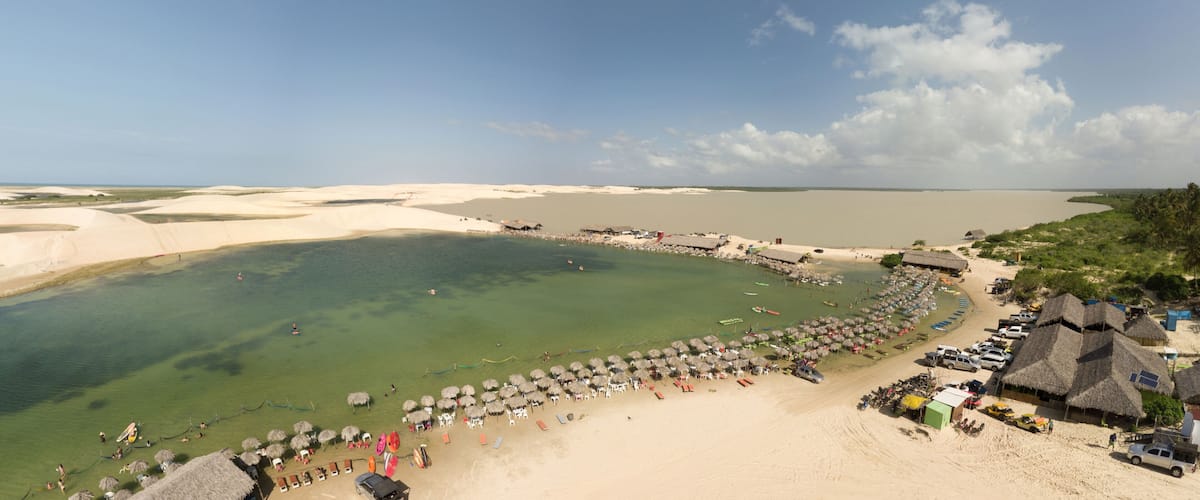 A coastal beach with clear waters, thatched-roof huts, and a sandy shoreline.