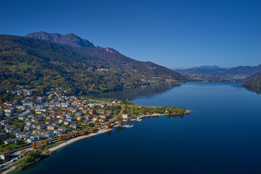 Aerial view of Lake Caldonazzo north of Italy. In the background the trees, Alps, blue sky. Reflection of mountains in water. Autumn season. Multi-colored palette of colors