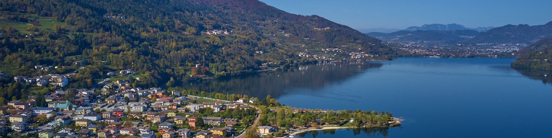 Aerial view of Lake Caldonazzo north of Italy. In the background the trees, Alps, blue sky. Reflection of mountains in water. Autumn season. Multi-colored palette of colors