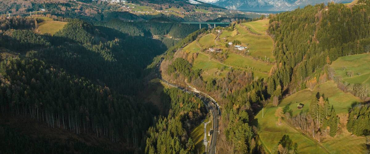 A mountainous landscape with a bridge, forested valleys, and snow-capped peaks.