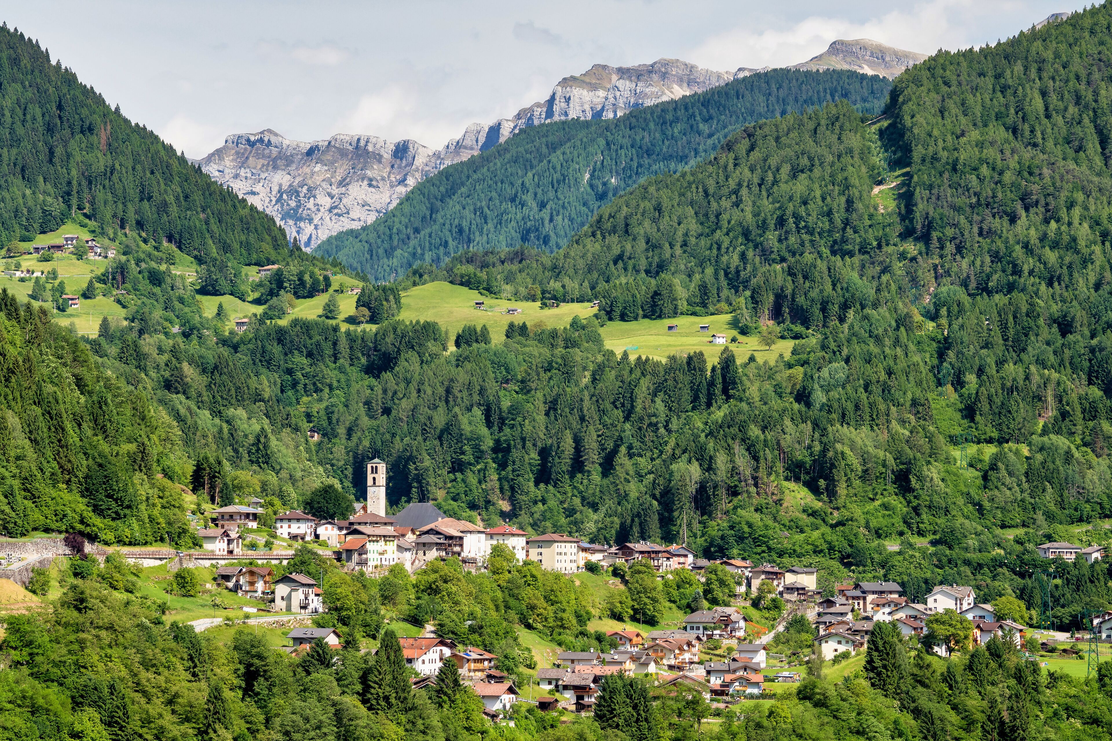 A mountainous village with houses nestled among dense forests and a prominent church tower.