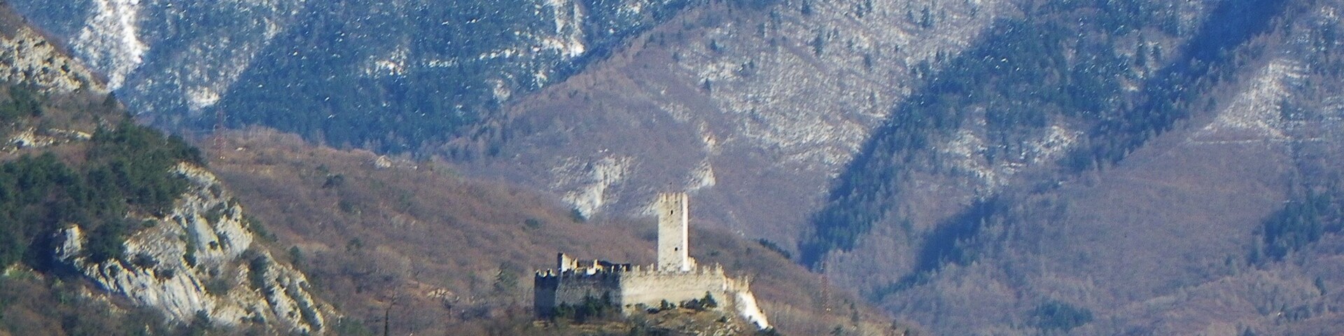 A castle on a hill with snow-capped mountains in the background.