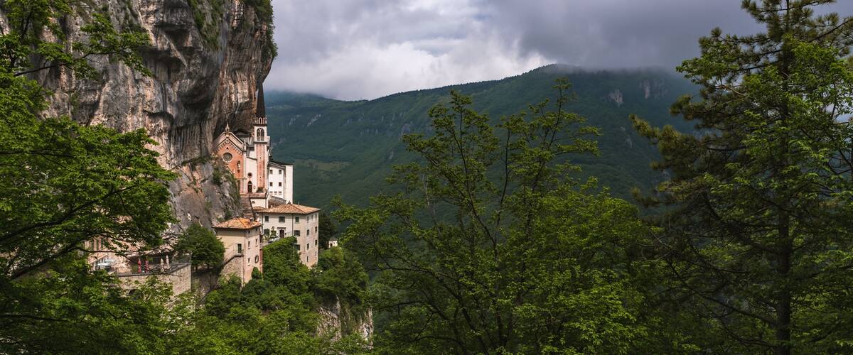 A monastery perched on a cliffside, surrounded by lush greenery and mountains.