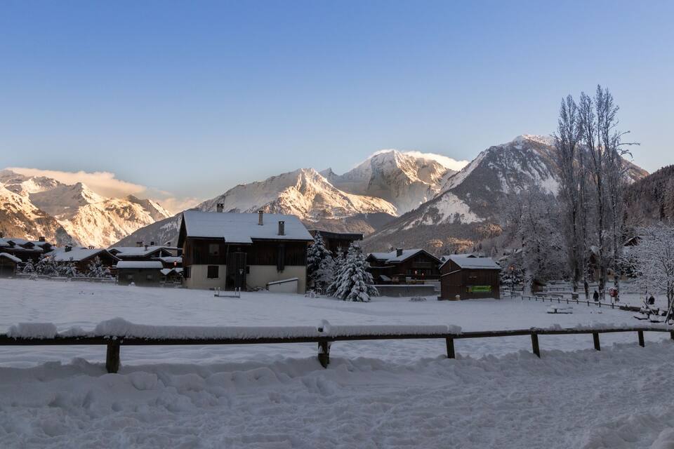 Un village enneigé, avec des maisons en bois et une chaîne de montagnes en arrière-plan.