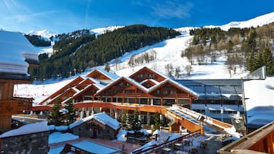 A snow-covered lodge with wooden architecture, a ski slope, and a mountain backdrop.