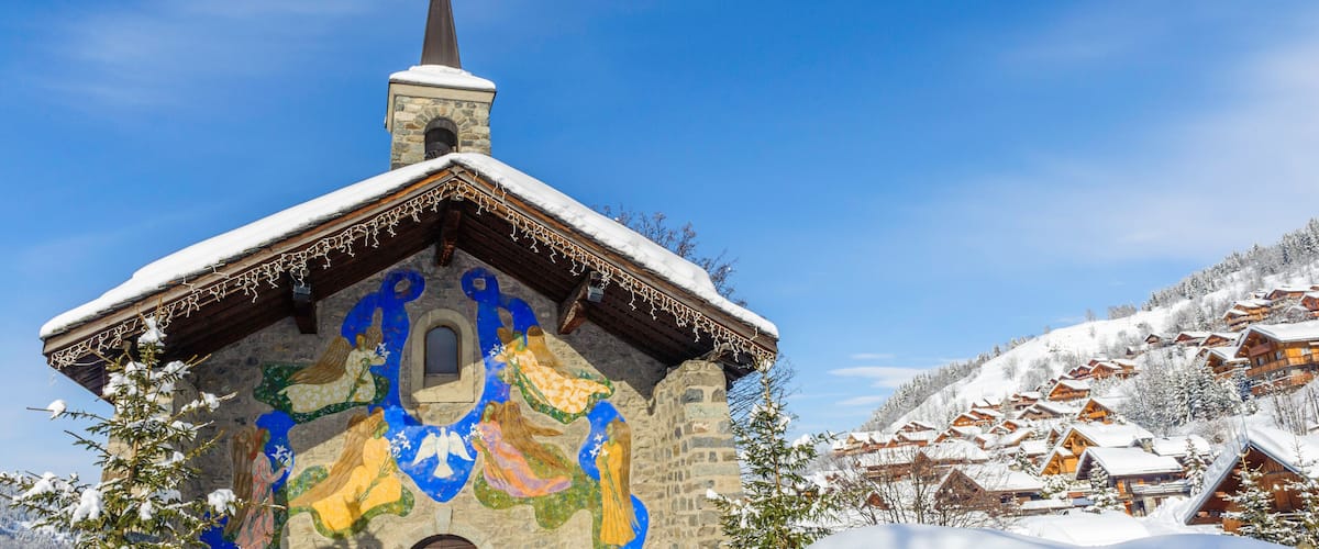 A snow-covered church with a colorful mural on its facade, surrounded by a snowy village.
