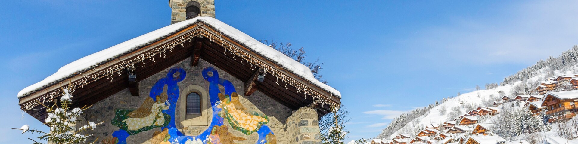 A snow-covered church with a colorful mural on its facade, surrounded by a snowy village.