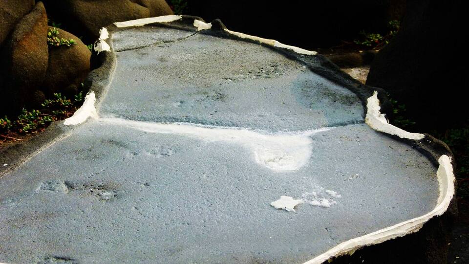 A concrete surface with irregular edges and patches of white material.