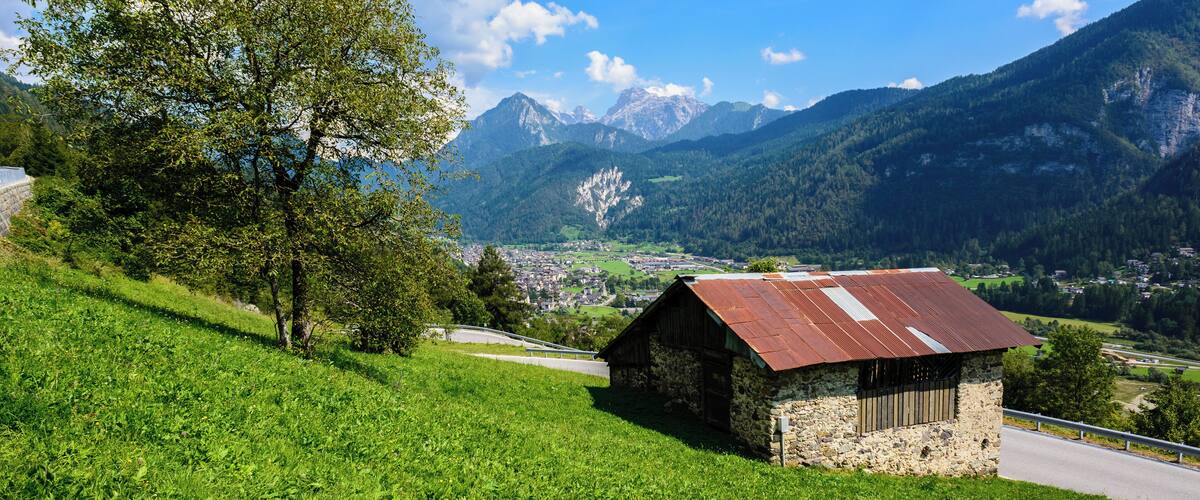 A mountain landscape with a small stone building, lush green fields, and a clear blue sky.