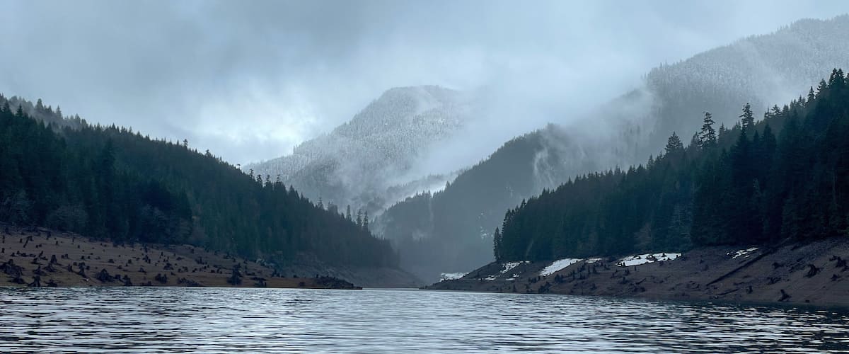 A river flanked by dense forests and mist-covered mountains.