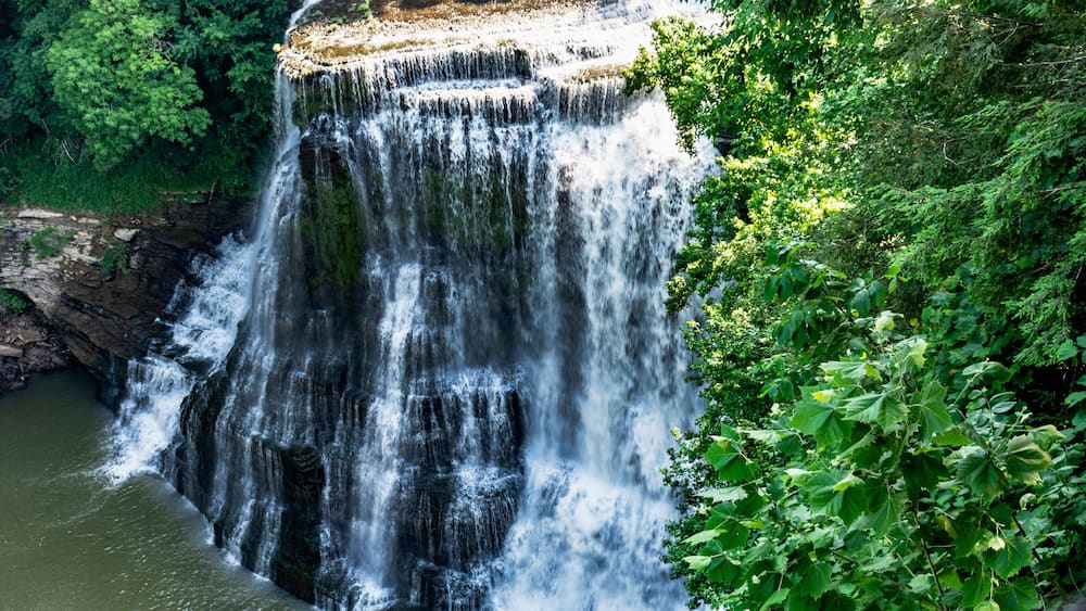 A waterfall cascading down a rocky cliff surrounded by lush greenery.