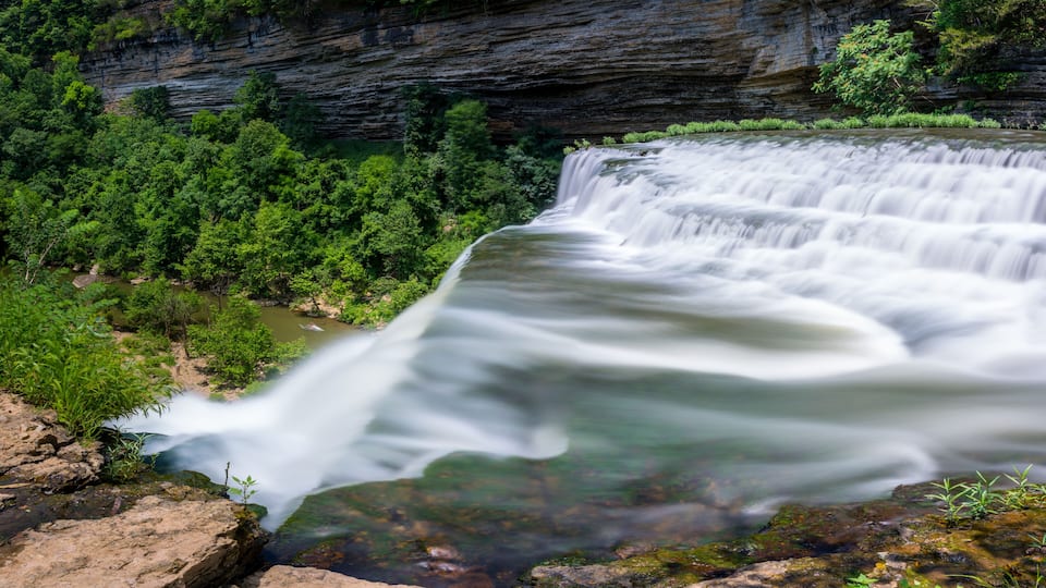 A waterfall cascading over a rocky cliff surrounded by lush greenery.
