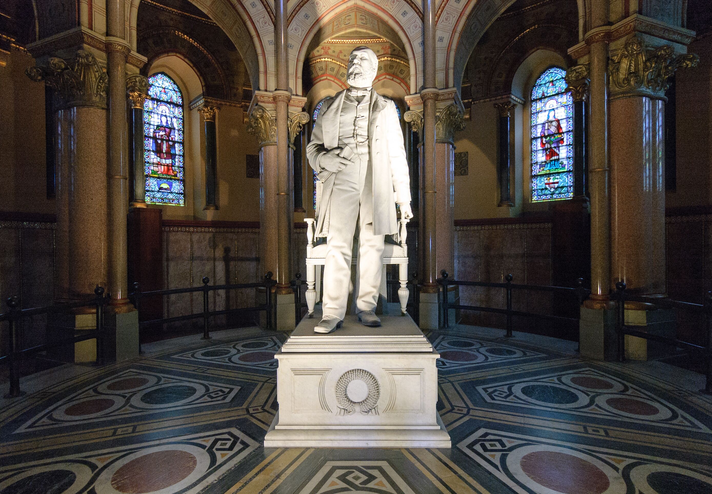 A statue in a church with stained glass windows and ornate columns.