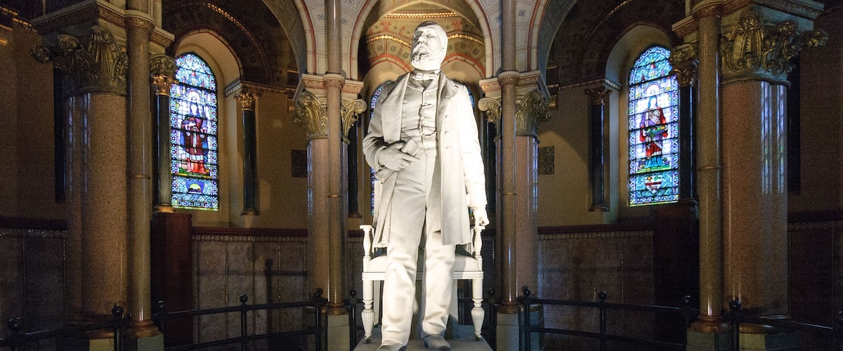 A statue in a church with stained glass windows and ornate columns.