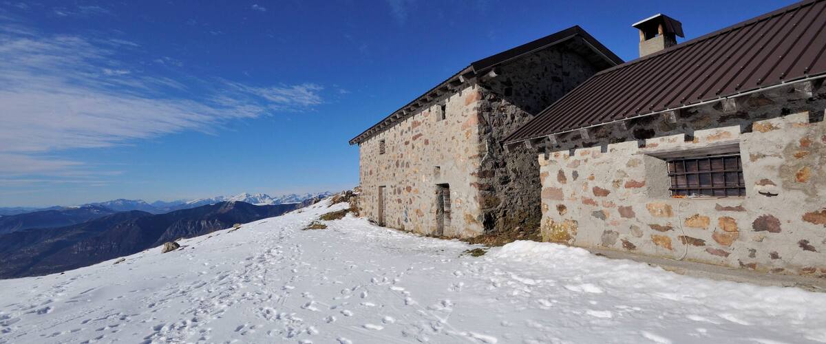 A snow-covered mountain path with a stone building and a metal roof.