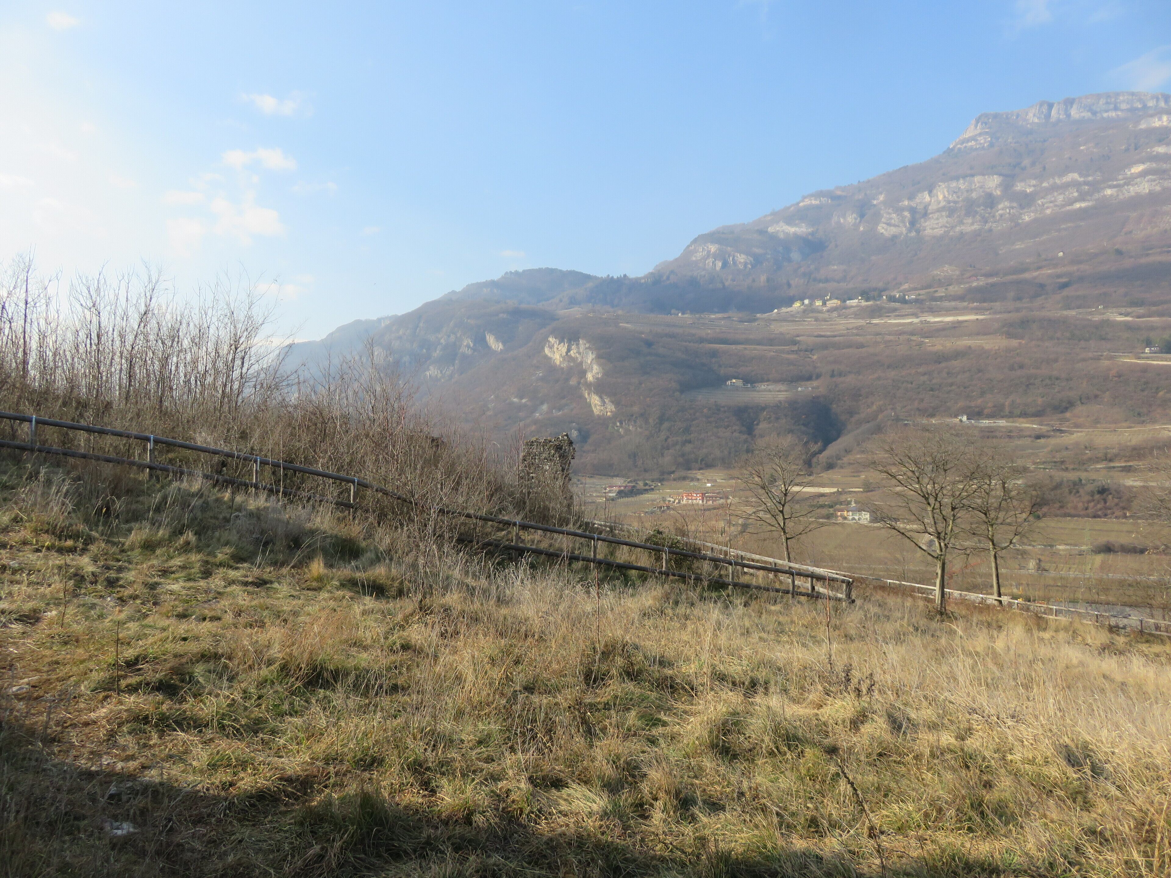 A mountainous landscape with a fence in the foreground and a village in the valley below.