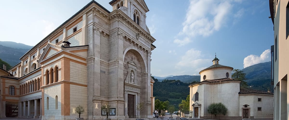 A historic church with a tall spire and a smaller dome, surrounded by cobblestone streets and greenery.
