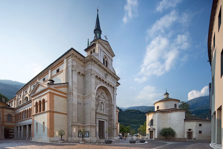 A historic church with a tall spire and a smaller dome, surrounded by cobblestone streets and greenery.