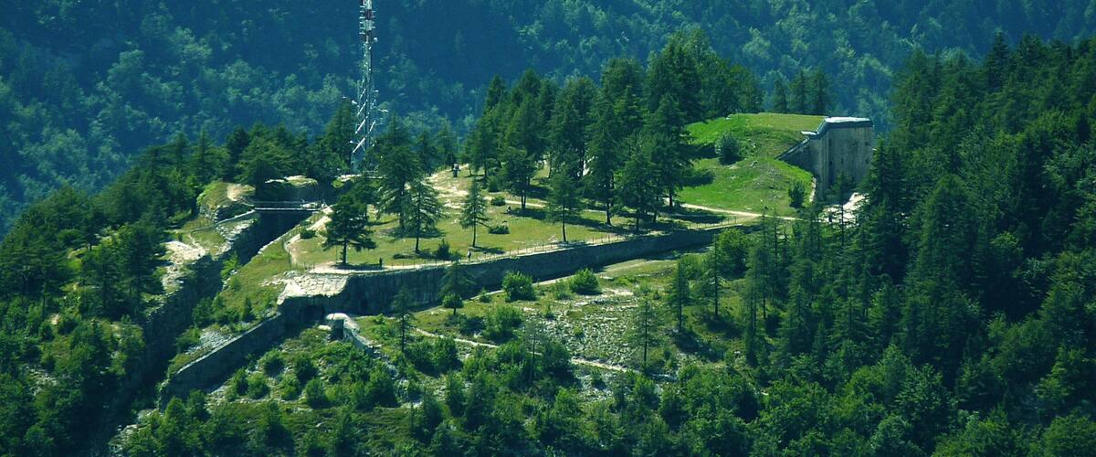 A mountainous landscape with a stone structure, a tall communication tower, and a small building surrounded by dense forest.
