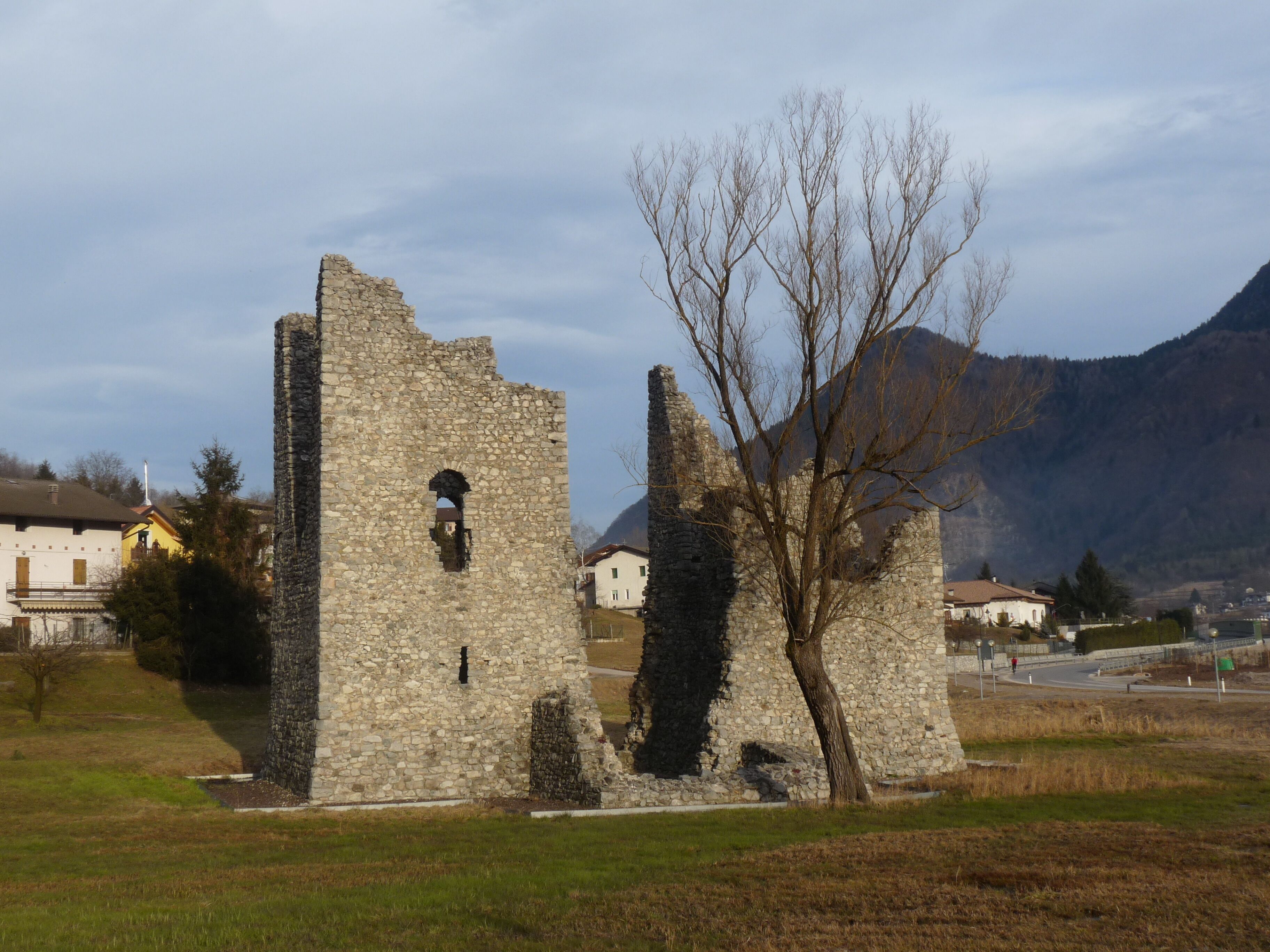 A stone ruin with a tree in front, set against a mountainous backdrop.