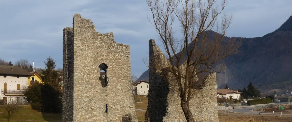 A stone ruin with a tree in front, set against a mountainous backdrop.