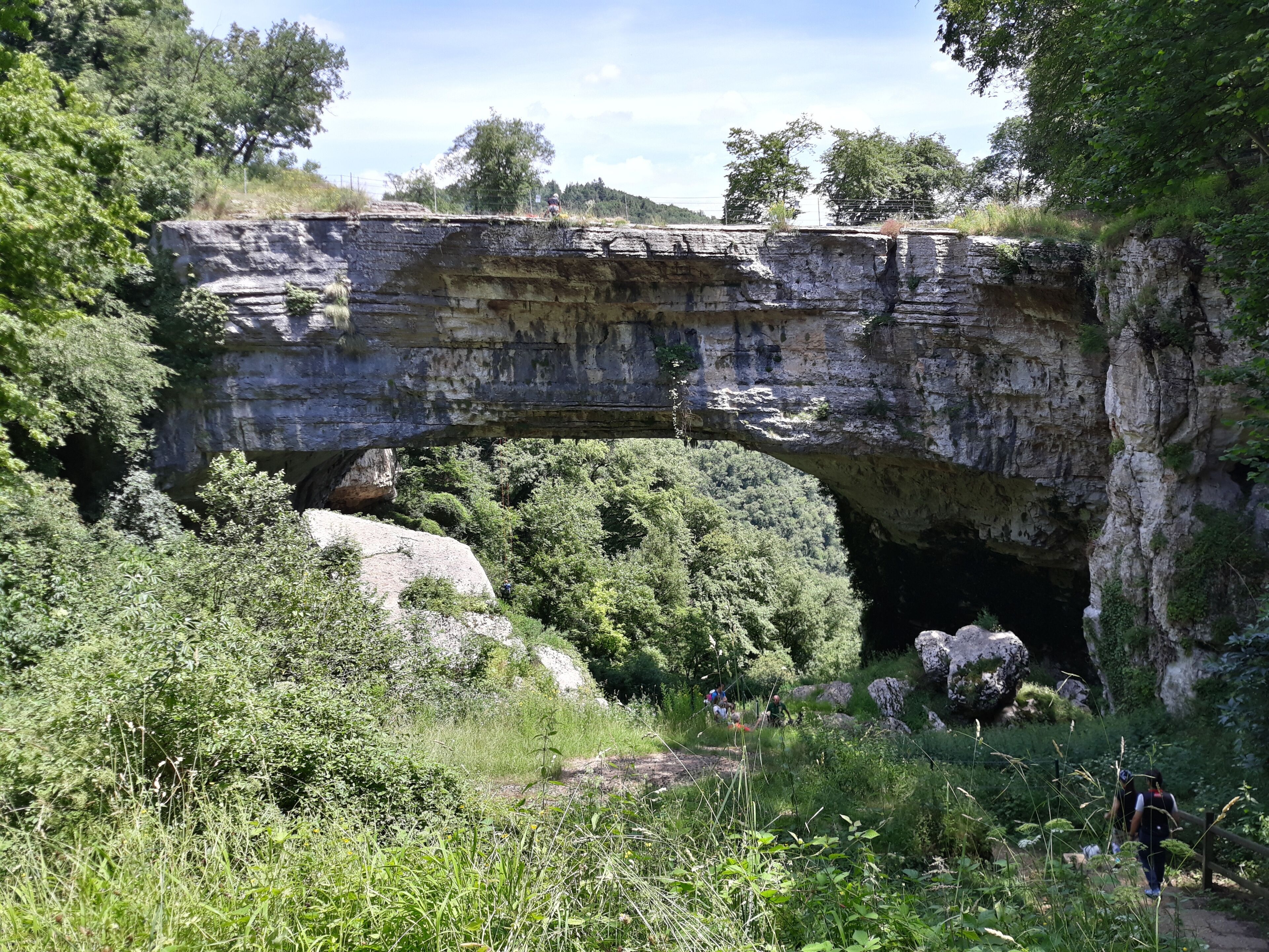 A natural rock arch formation with hikers below.