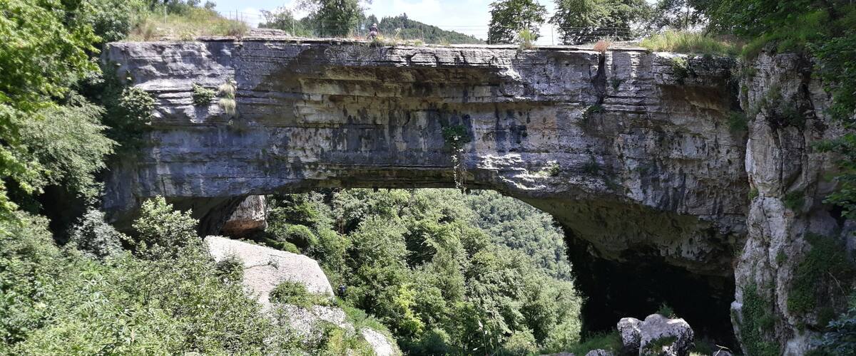 A natural rock arch formation with hikers below.