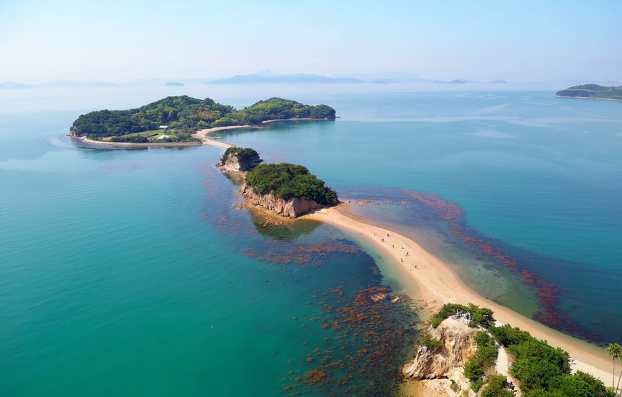 An aerial view of a coastal area with a sandy beach, clear turquoise waters, and green islands.