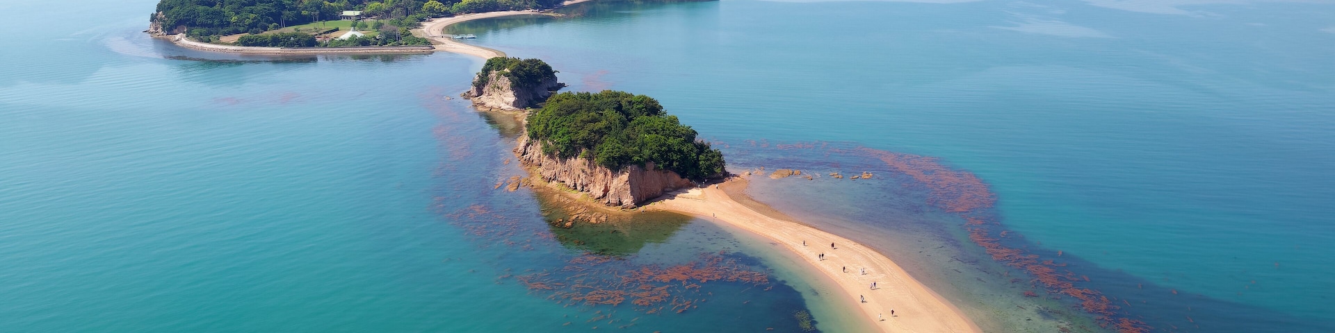 An aerial view of a coastal area with a sandy beach, clear turquoise waters, and green islands.