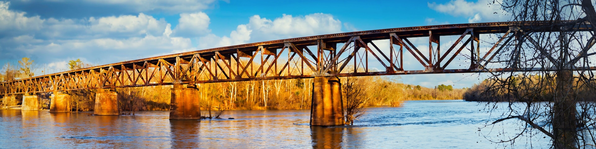 Eine Stahlbrücke über einem Fluss, mit Herbstlaub und blauem Himmel.