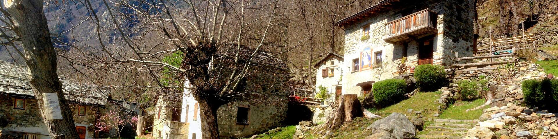 A stone house with a wooden balcony, surrounded by a mountainous landscape and a clear blue sky.