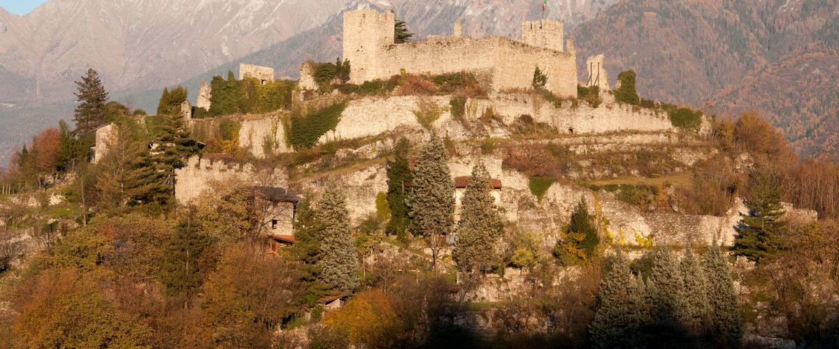 A historic castle on a hill with mountains in the background.