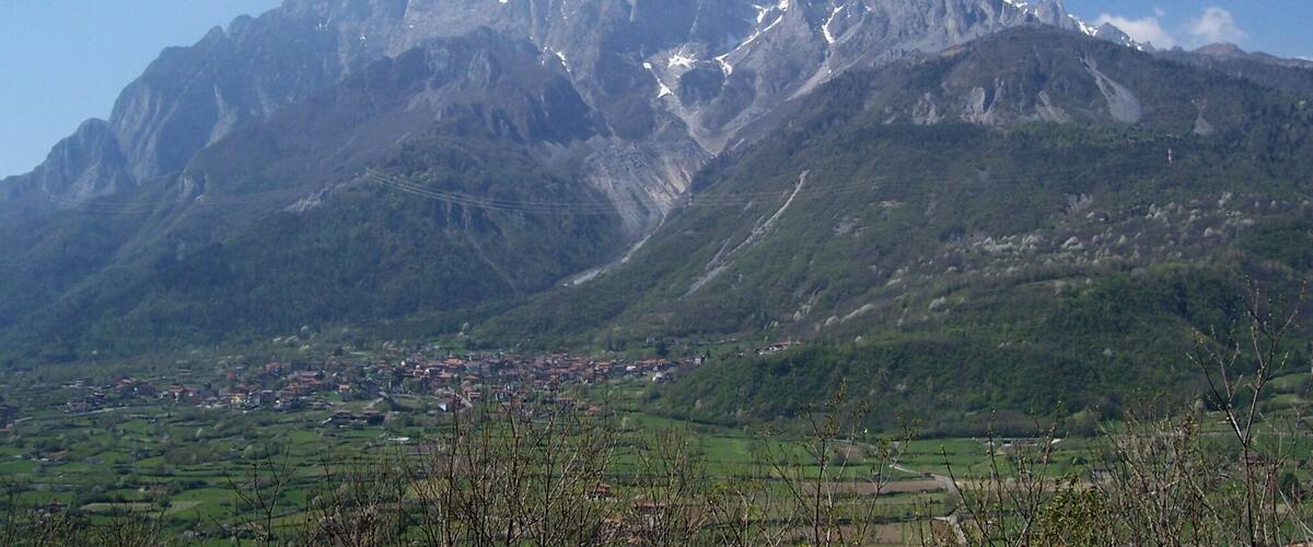 A mountain range with snow-capped peaks and a valley with scattered buildings.