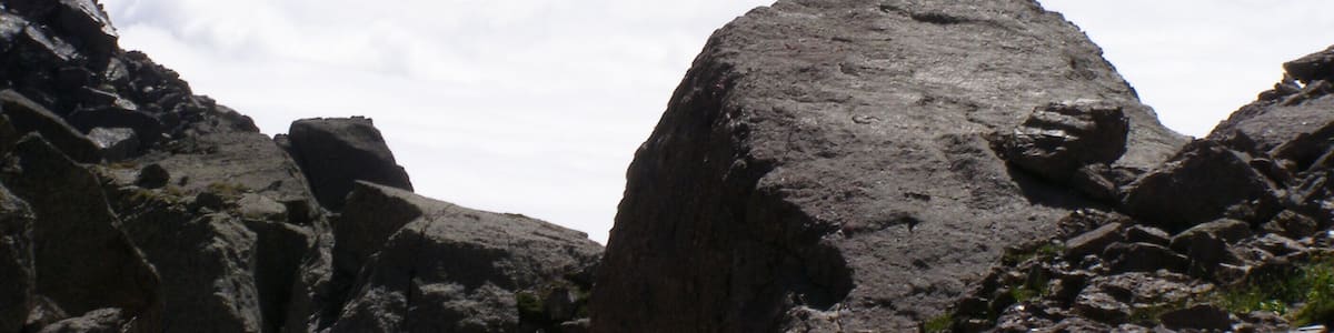 A rocky mountain landscape with prominent boulders and a range of mountains in the background.
