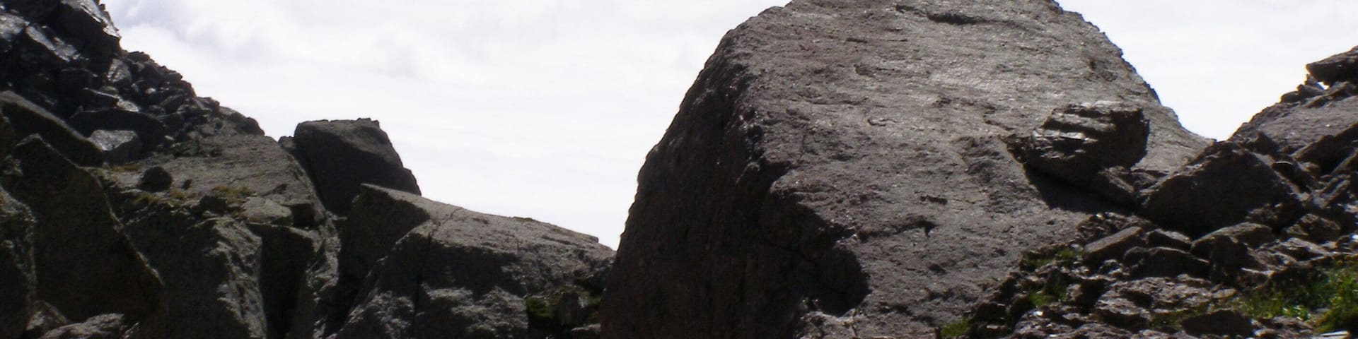 A rocky mountain landscape with prominent boulders and a range of mountains in the background.
