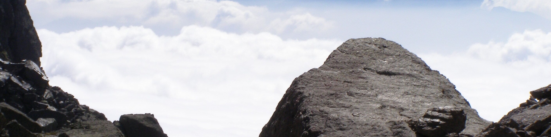 A rocky mountain landscape with prominent boulders and a range of mountains in the background.