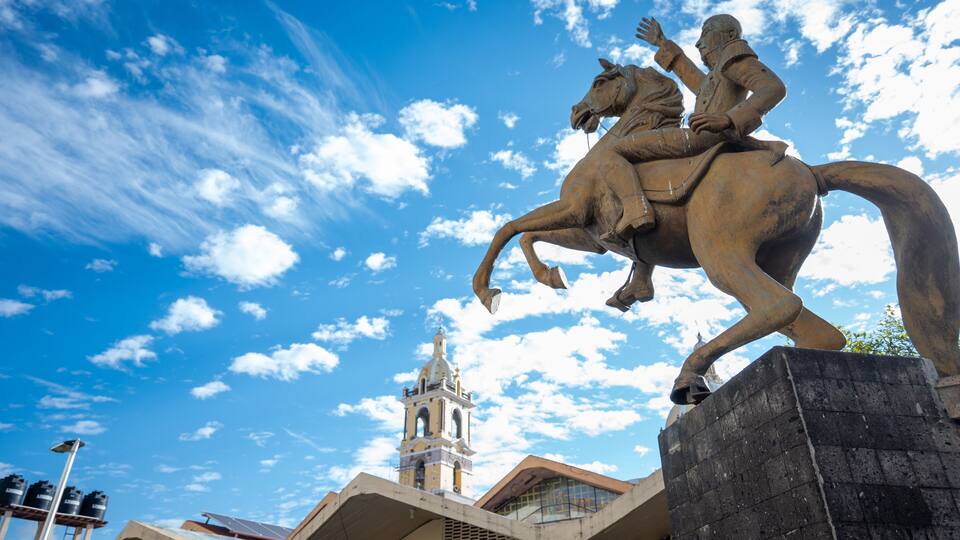 A statue of a man on a horse, a clock tower, and a clear blue sky with clouds.