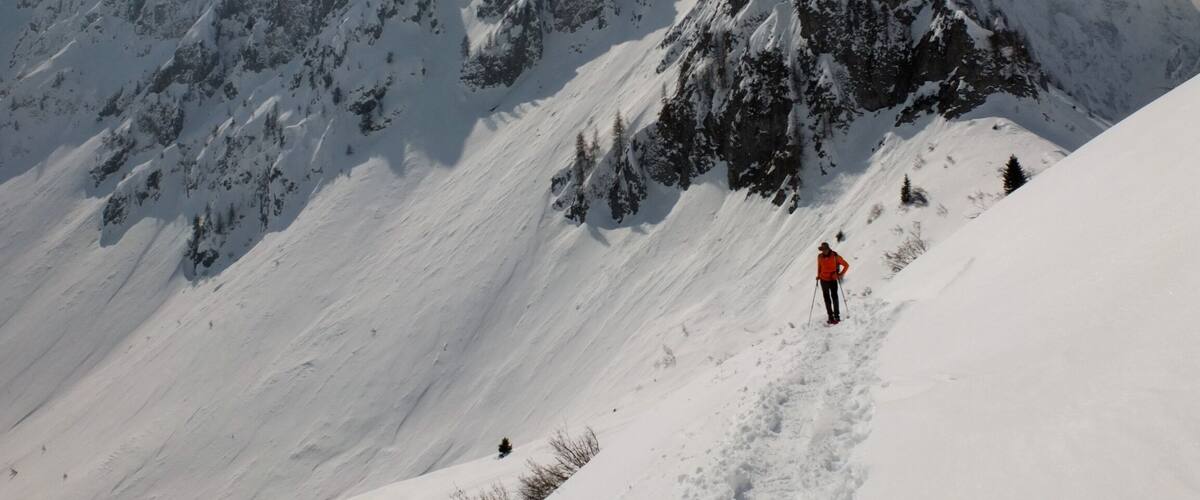 A snow-covered mountain range with a skier in a red jacket descending a slope.
